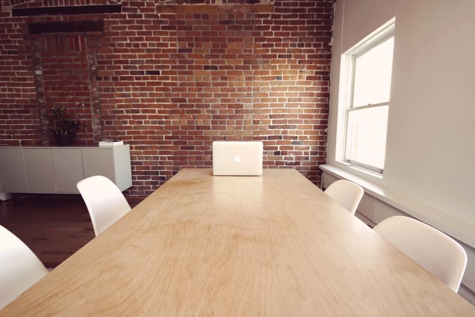 A bright meeting room with a long wooden table and a laptop