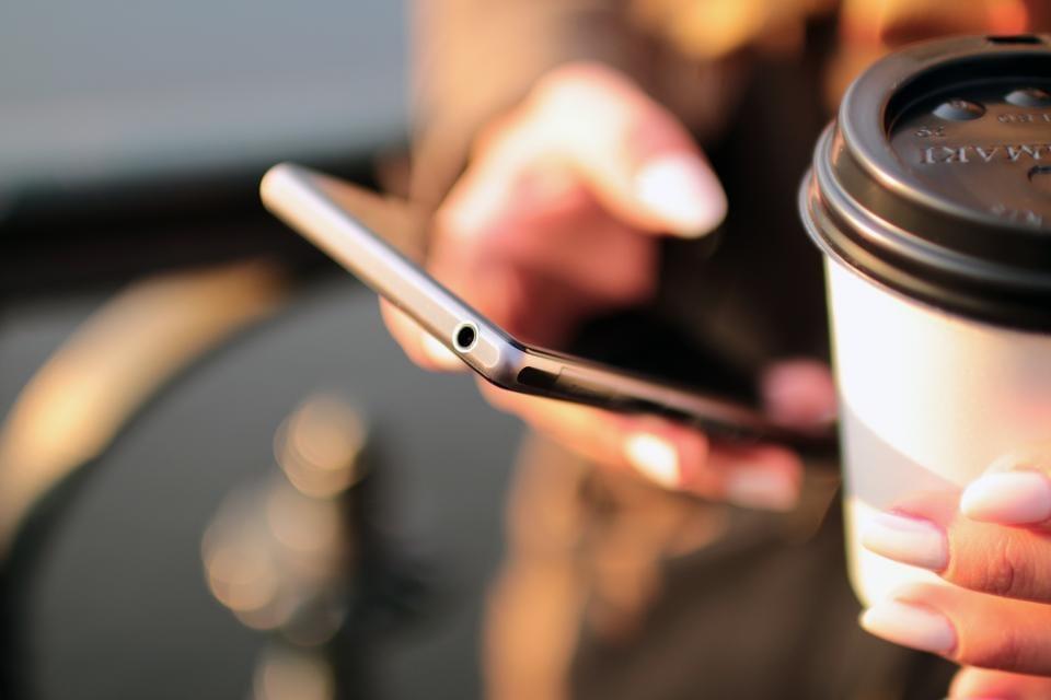 A person holding a smartphone and a coffee cup